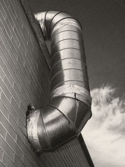 Round galvanised steel ductwork bending down the side of a brick wall.