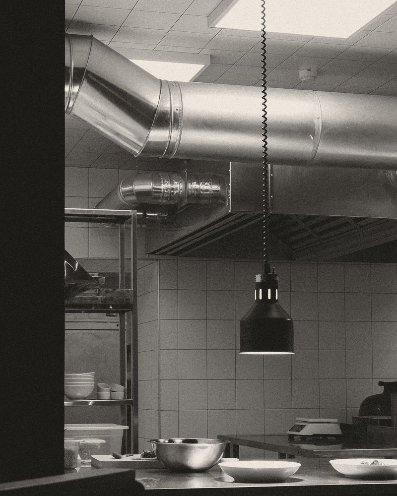 A commercial kitchen after service: steel ducting above a hood, a hanging heat lamp and an empty steel counter.
